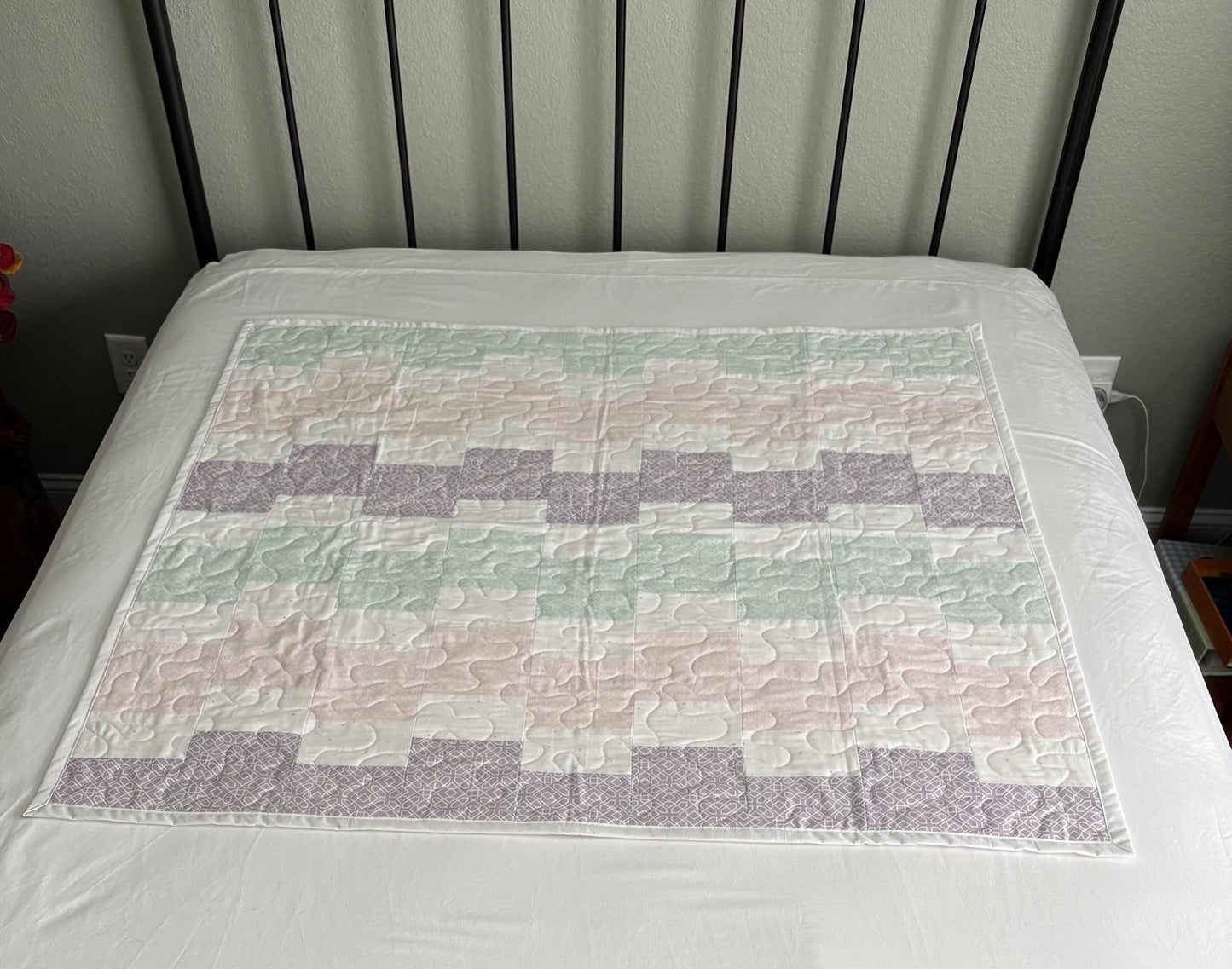 Quilt with a geometric pattern on a bed with a white sheet and black headboard.